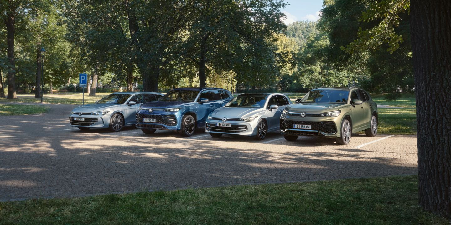 Vier VW Plug-In-Hybrid-Modelle stehen nebeneinander auf einem Parkplatz in einem Park.