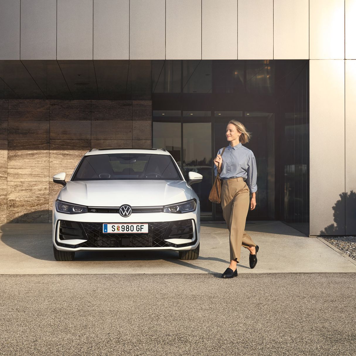 Frontansicht eines weißen VW Passat R-Line, eine Frau geht an ihm vorbei.