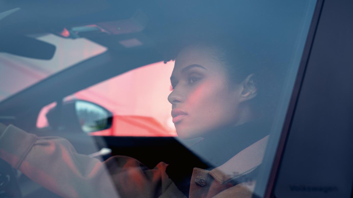 Blick durch das Fenster auf der Fahrerseite eines VW ID.4 GTX. Innen sitzt eine junge Frau und schaut hinaus.