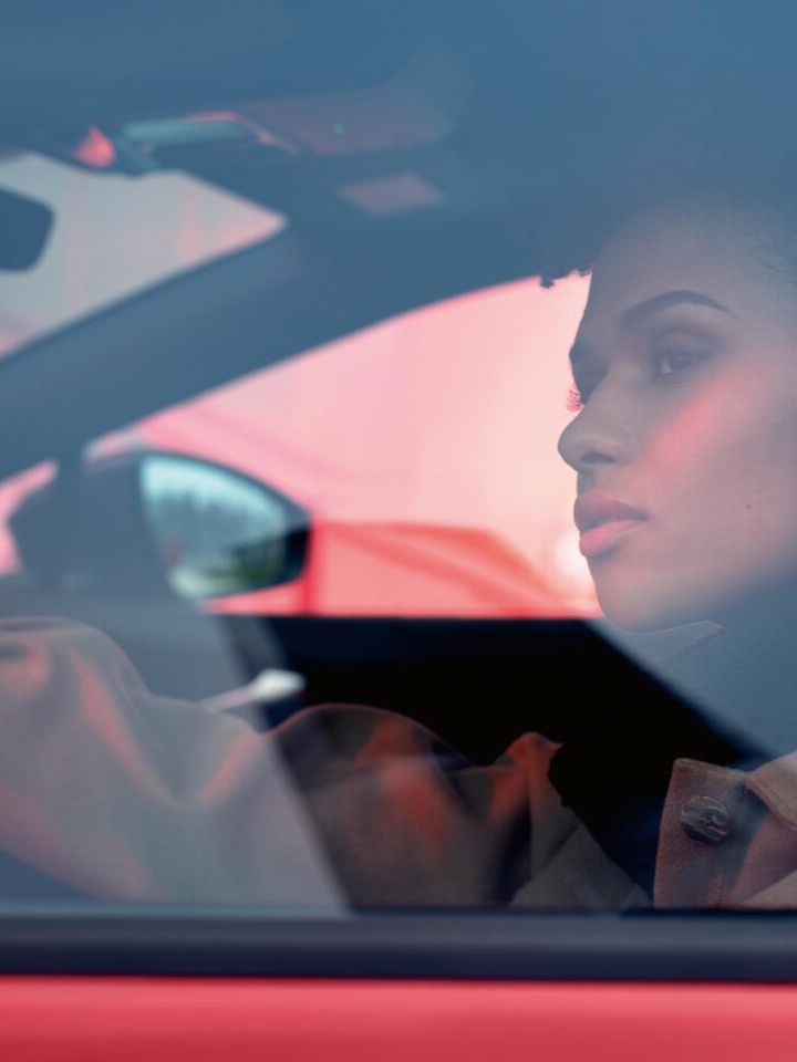 Blick durch das Fenster auf der Fahrerseite eines VW ID.4 GTX. Innen sitzt eine junge Frau und schaut hinaus.