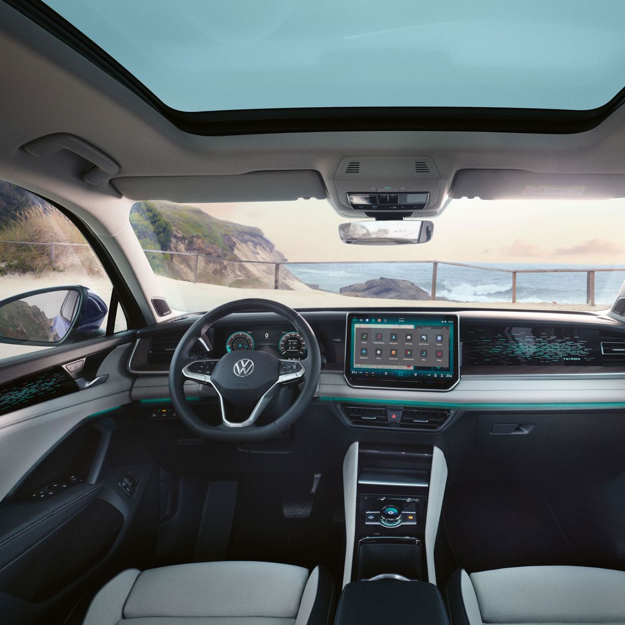 Blick auf das Cockpit mit Lenkrad und Infotainment-System im VW Tayron mit Aussicht auf eine Klippe und Meer.