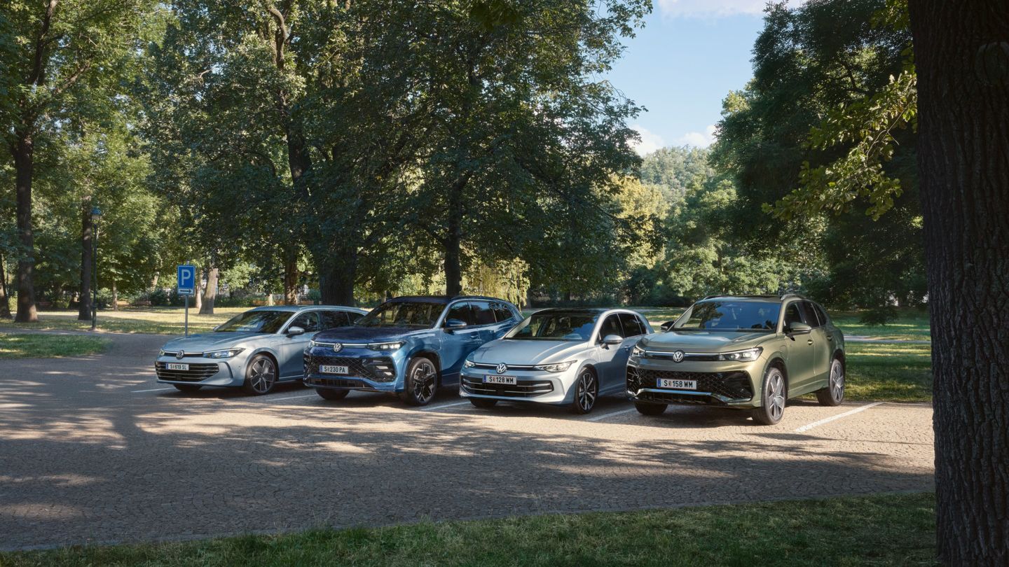 Vier VW Plug-In-Hybrid-Modelle stehen nebeneinander auf einem Parkplatz in einem Park.