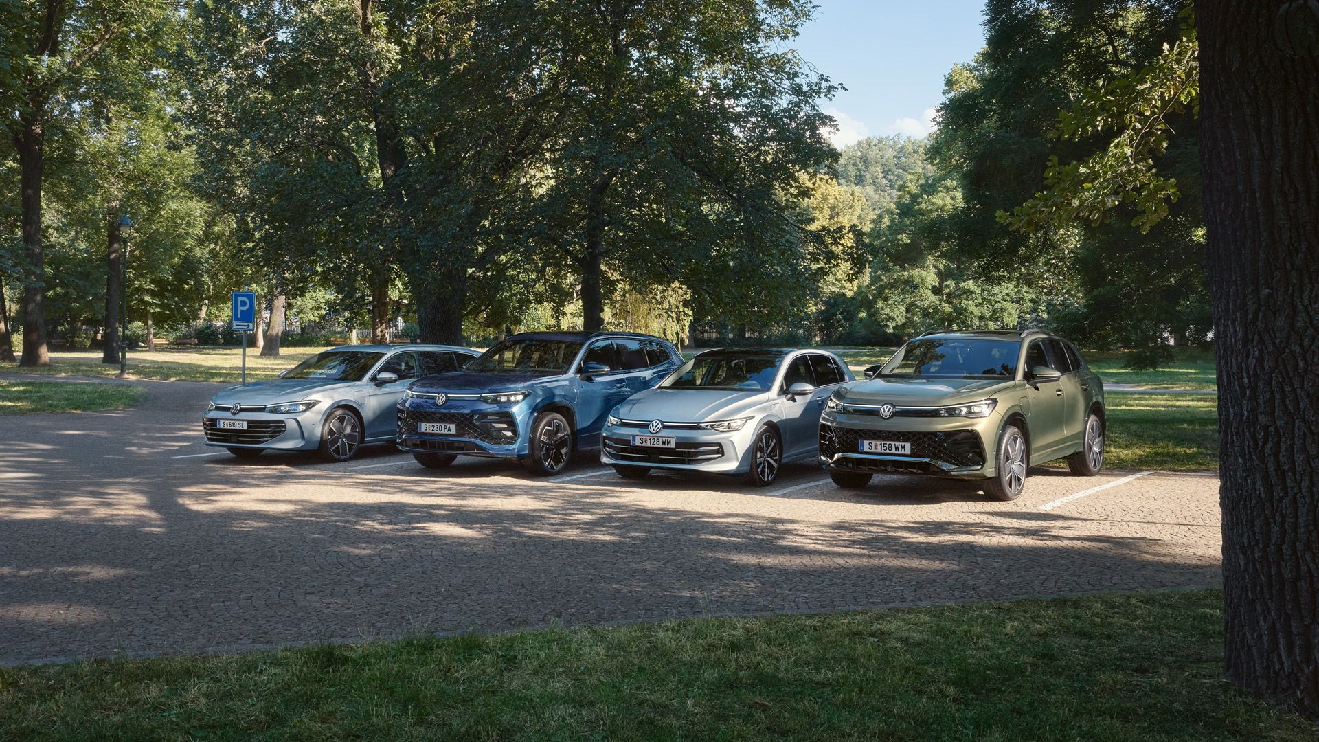 Vier VW Plug-In-Hybrid-Modelle stehen nebeneinander auf einem Parkplatz in einem Park.