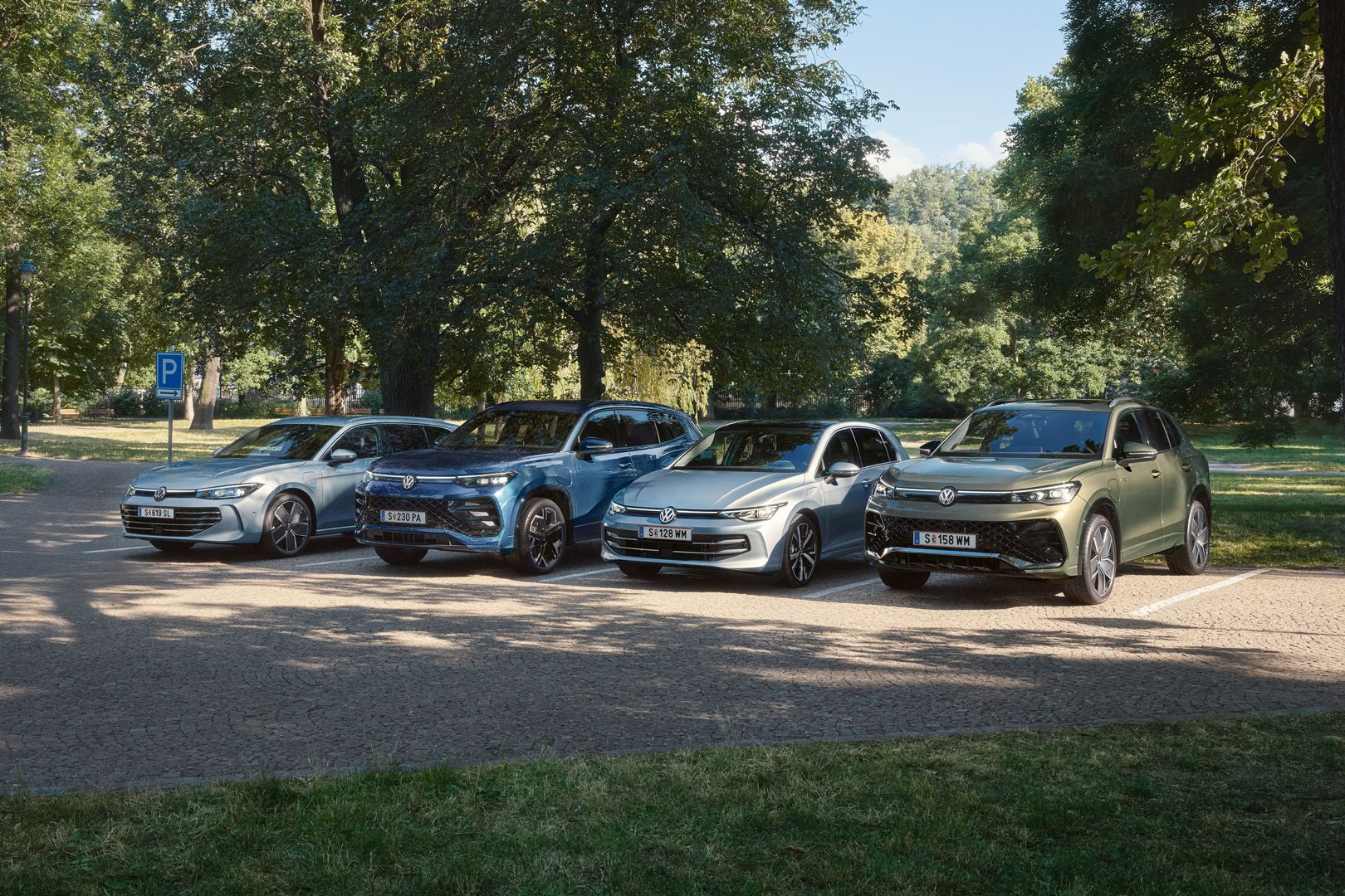 Vier VW Plug-In-Hybrid-Modelle stehen nebeneinander auf einem Parkplatz in einem Park.