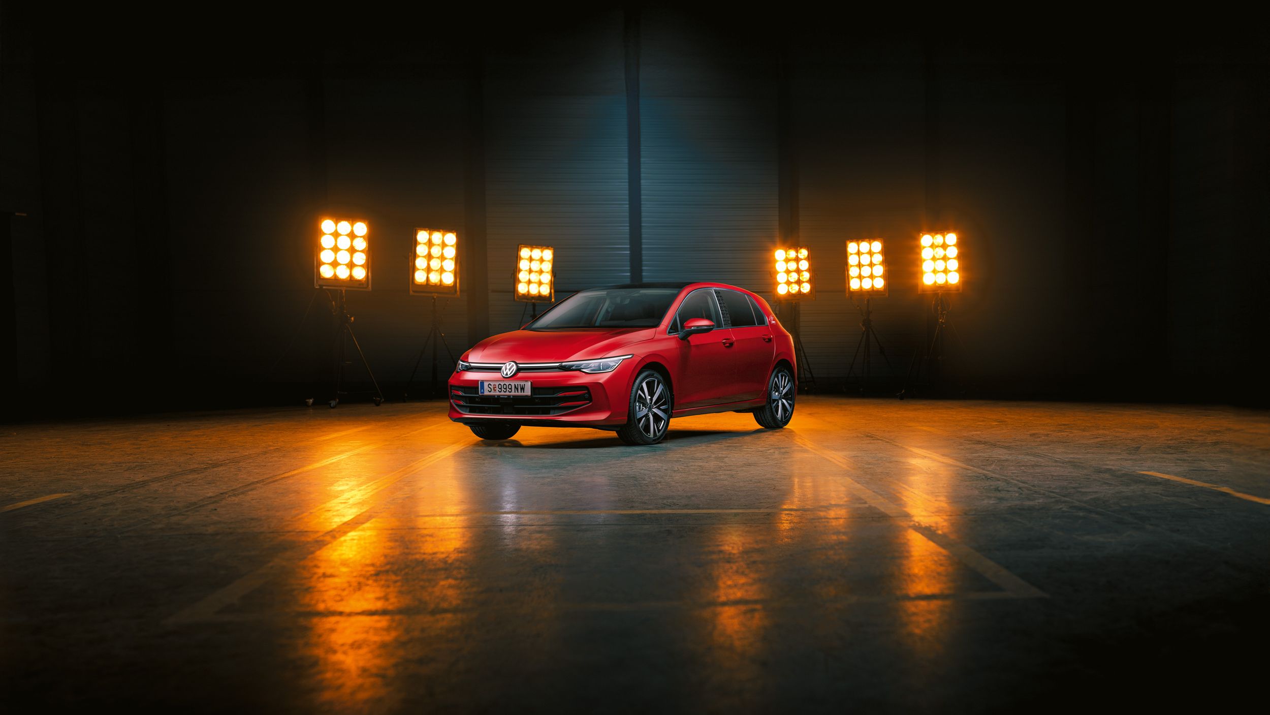 Ein roter Der VW Golf Falco Edition steht einer leeren Halle, dahinter Bühnenlicht.