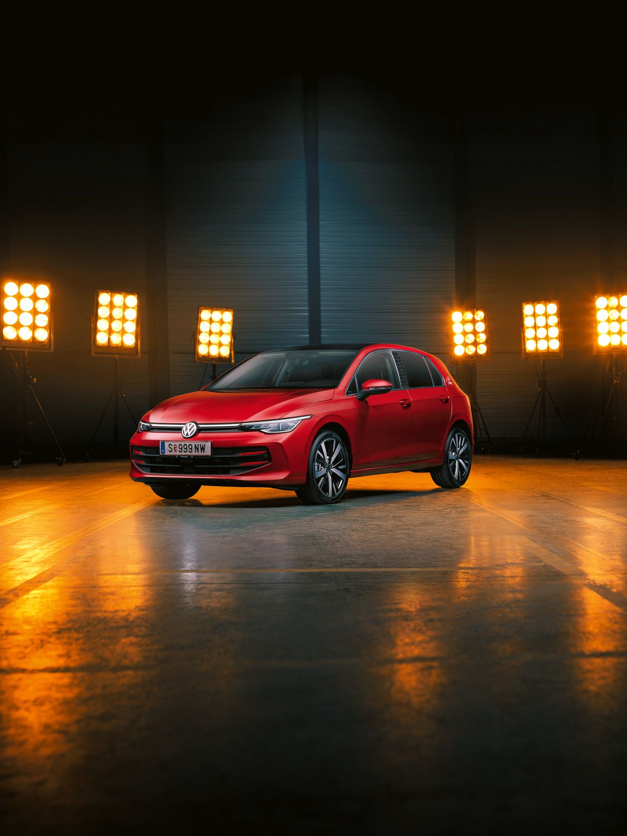 Ein roter Der VW Golf Falco Edition steht einer leeren Halle, dahinter Bühnenlicht.