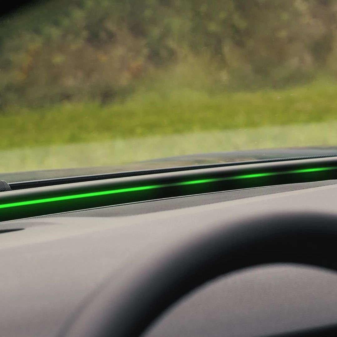 Das Bild zeigt eine grüne LED-Leiste, die auf dem Armaturenbrett eines Autos installiert ist. Im Hintergrund sieht man eine verschwommene Landschaft mit Gras. Die LED-Leiste leuchtet in einem kräftigen Grün.