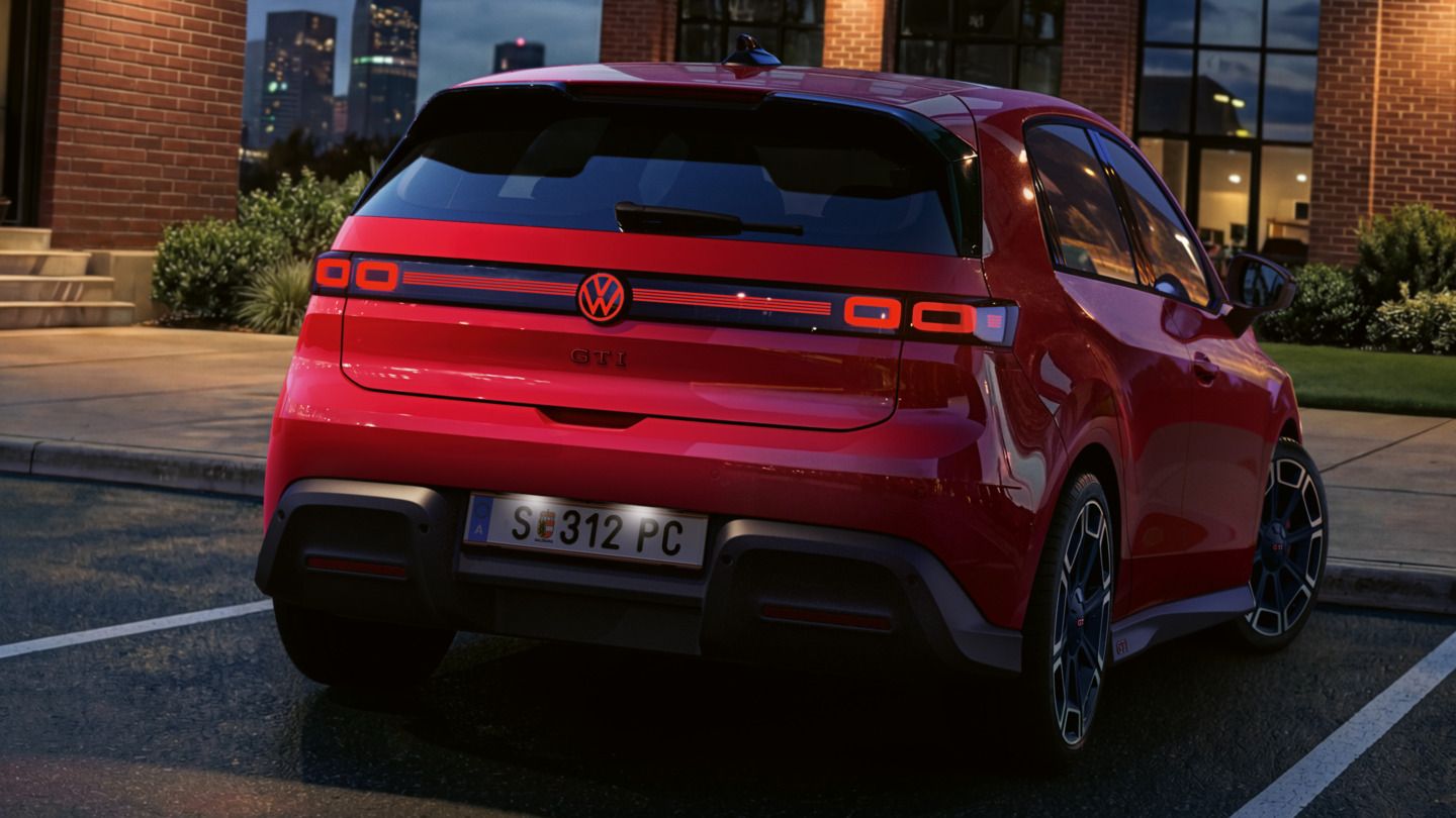 Heckansicht eines roten VW ID. Polo GTI mit eingeschalteten Rückleuchten und beleuchtetem Logo, der vor einem Bürogebäude parkt.