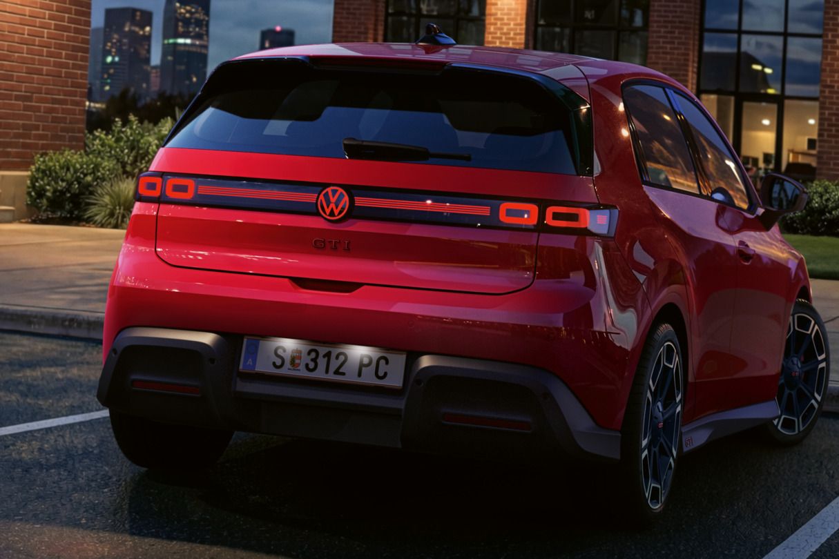 Heckansicht eines roten VW ID. Polo GTI mit eingeschalteten Rückleuchten und beleuchtetem Logo, der vor einem Bürogebäude parkt.
