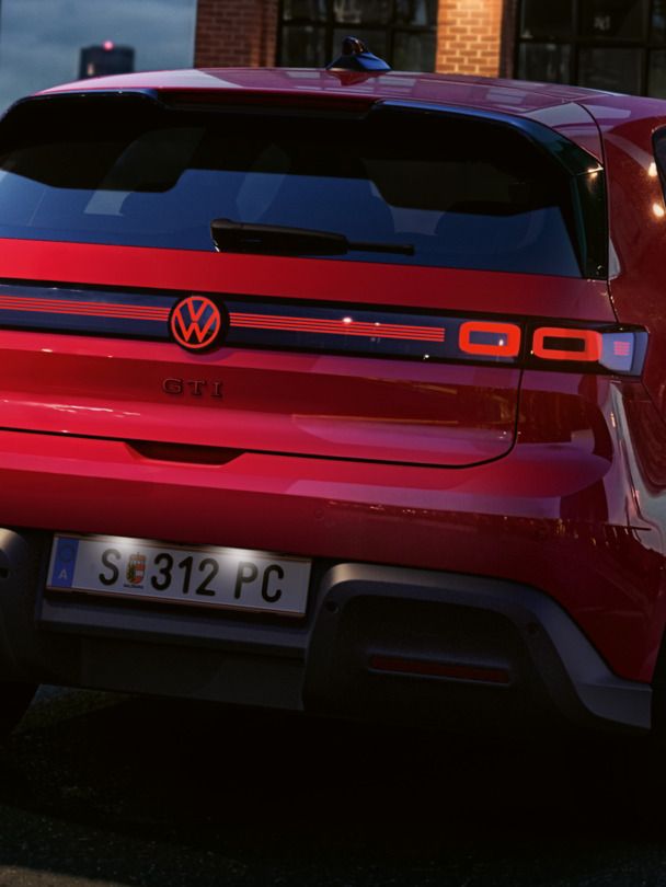 Heckansicht eines roten VW ID. Polo GTI mit eingeschalteten Rückleuchten und beleuchtetem Logo, der vor einem Bürogebäude parkt.