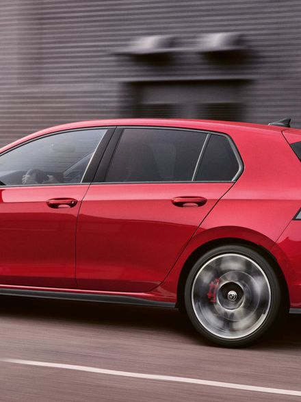 Ein roter VW Golf GTI fährt vor einer Lagerhalle entlang.