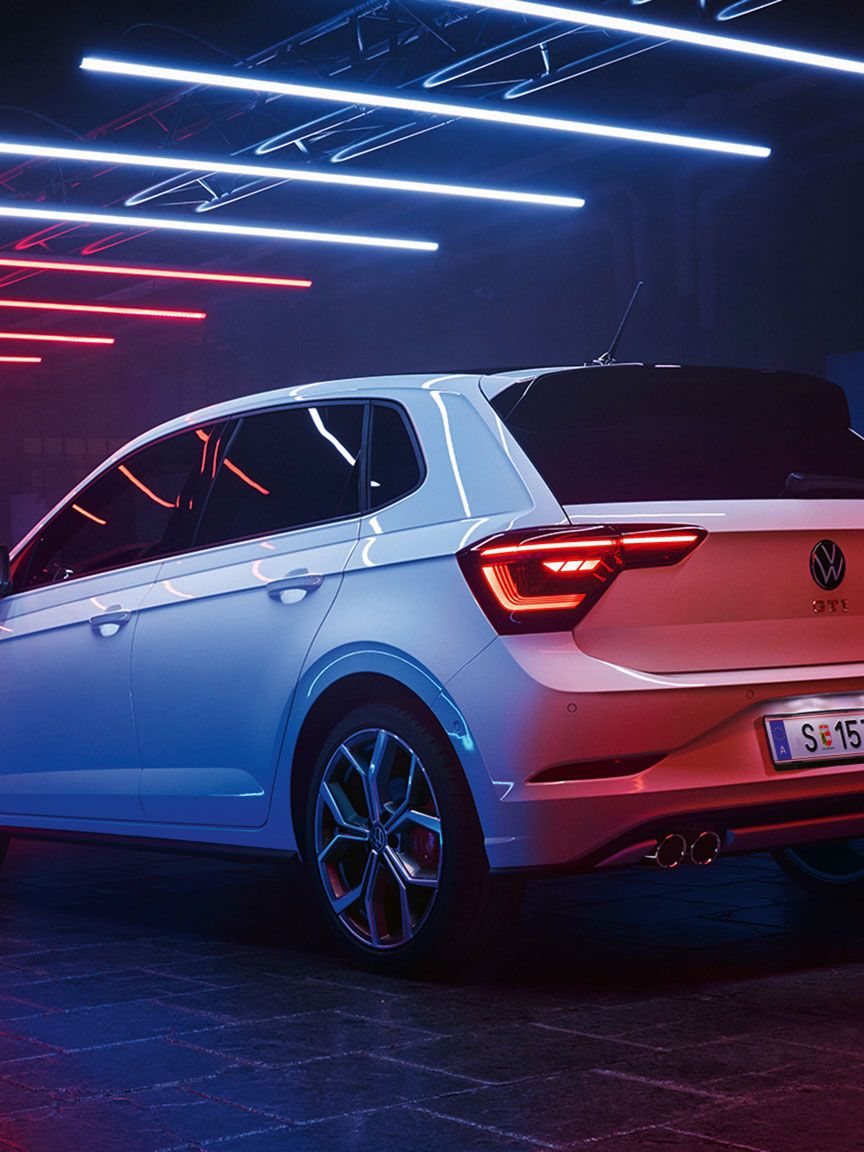 Ein weißer VW Polo GTI mit Design-Paket „Black Style“ steht in einer dunklen Halle, Leuchtstreifen reflektieren sich auf dem Lack.