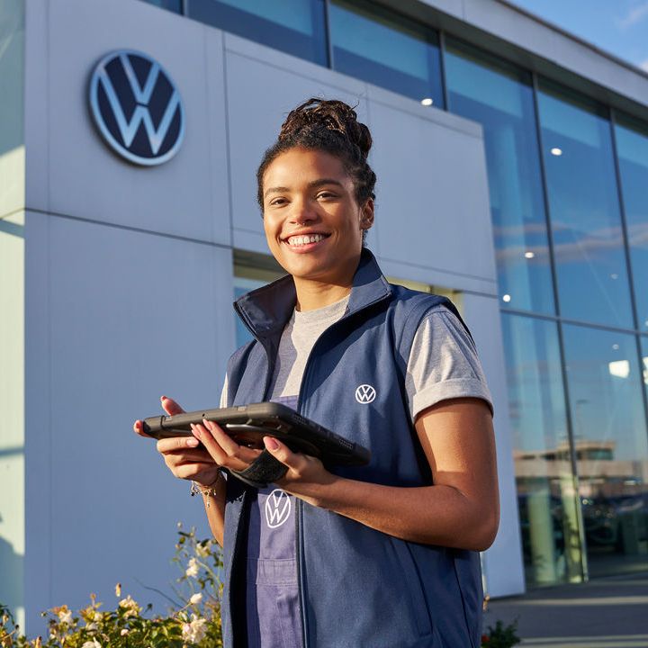 Servicefrau steht mit Tablet vor einem Volkswagen Partner Gebäude.