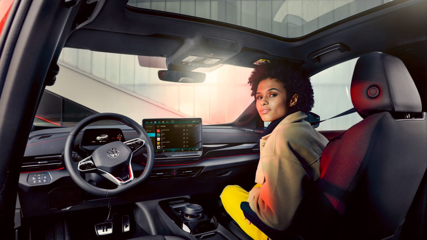 VW ID.4 GTX Innenraum mit Blick auf die Vordersitze und Cockpit. Frau sitzt auf Beifahrersitz mit Blick nach hinten.