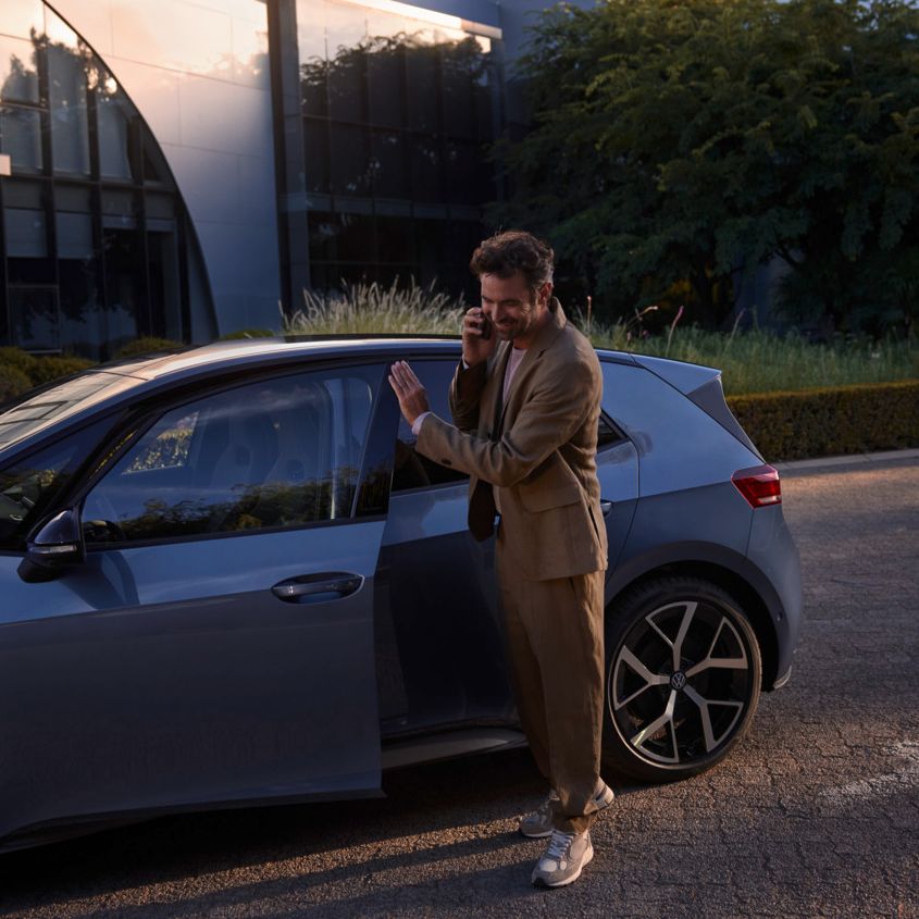 Ein Mann steht vor einem blauen VW ID.3 Neo und telefoniert per Smartphone