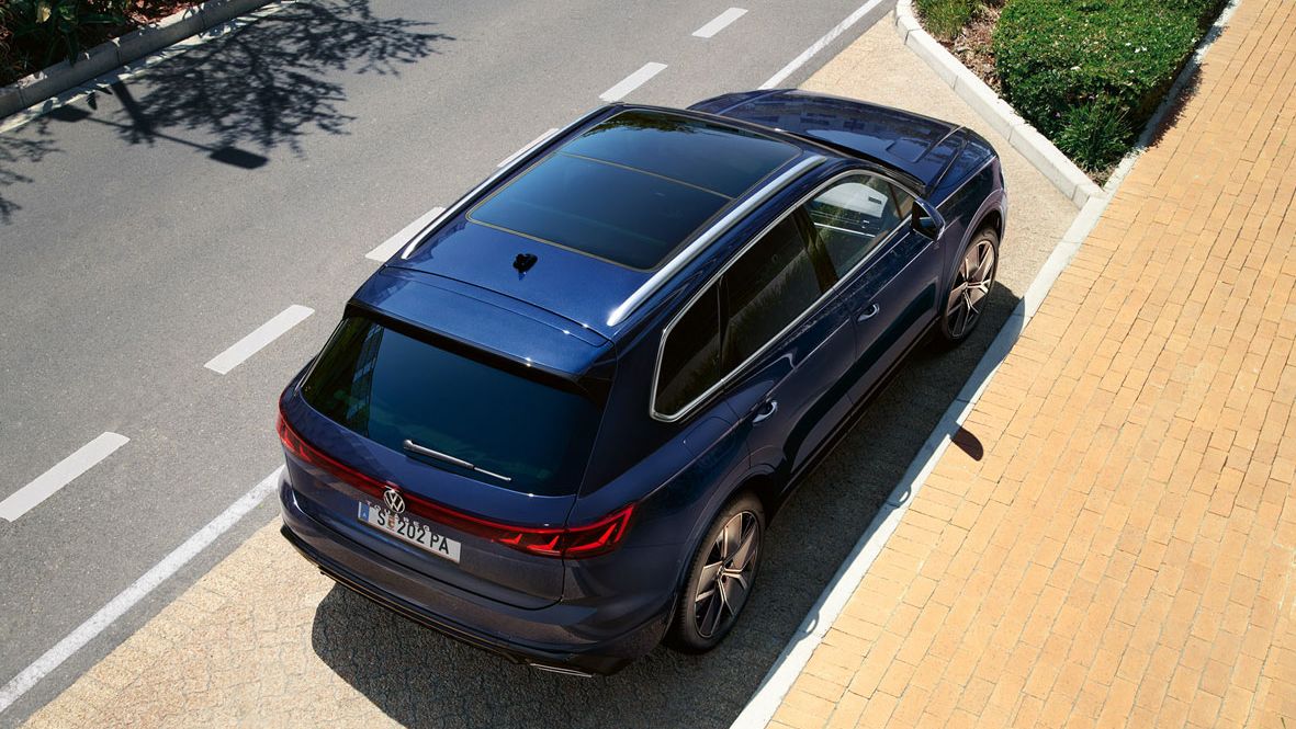 Ein VW Touareg R-Line parkt am Straßenrand, Ansicht von schräg oben auf das Heck und Panoramaglasdach.