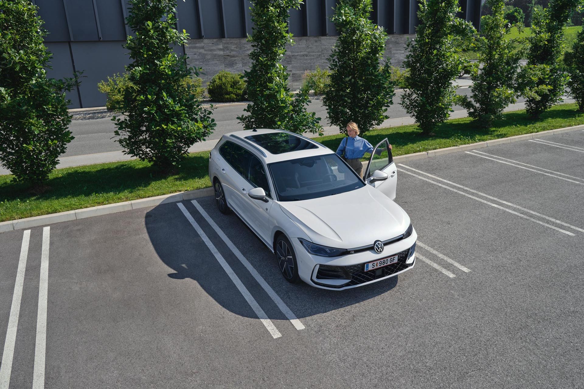 Weißer VW Passat parkt vor einem modernen Bürogebäude. Eine Frau steigt ein.
