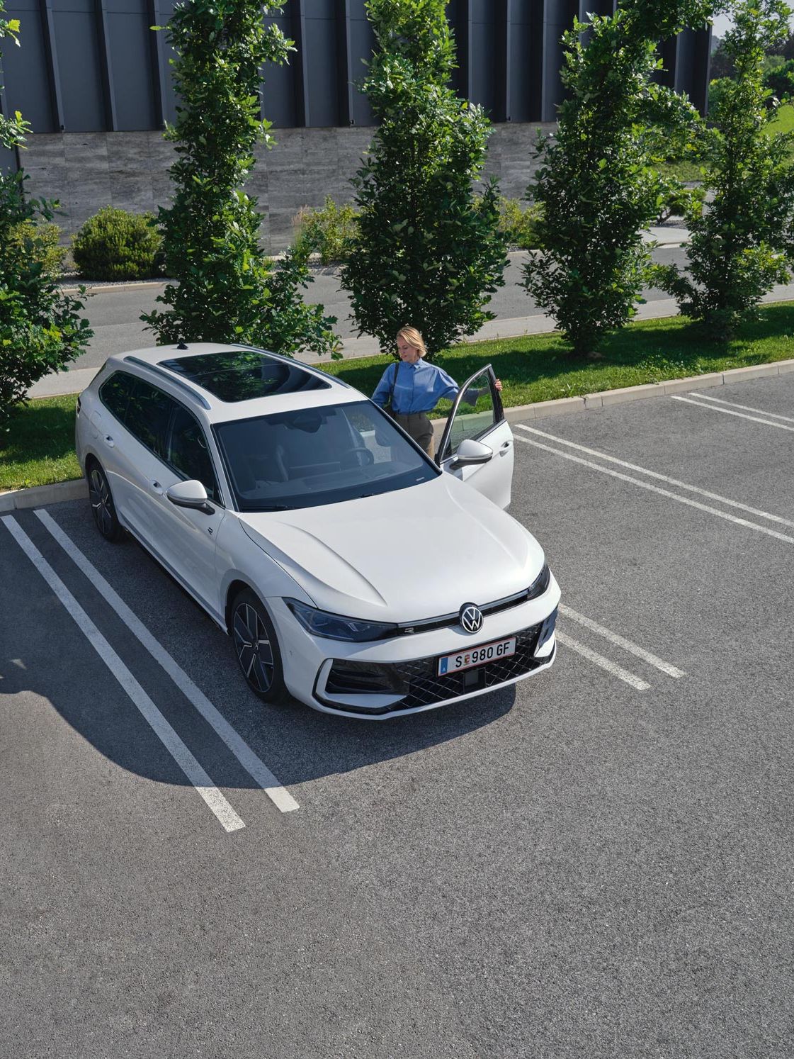 Weißer VW Passat parkt vor einem modernen Bürogebäude. Eine Frau steigt ein.