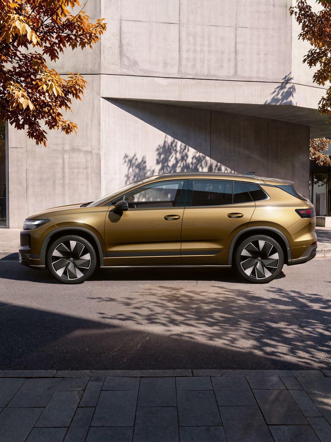 Seitenansicht eines oliv-bronzefarbenen VW ID.4 Reskin geparkt vor einem modernen Wohngebäude.