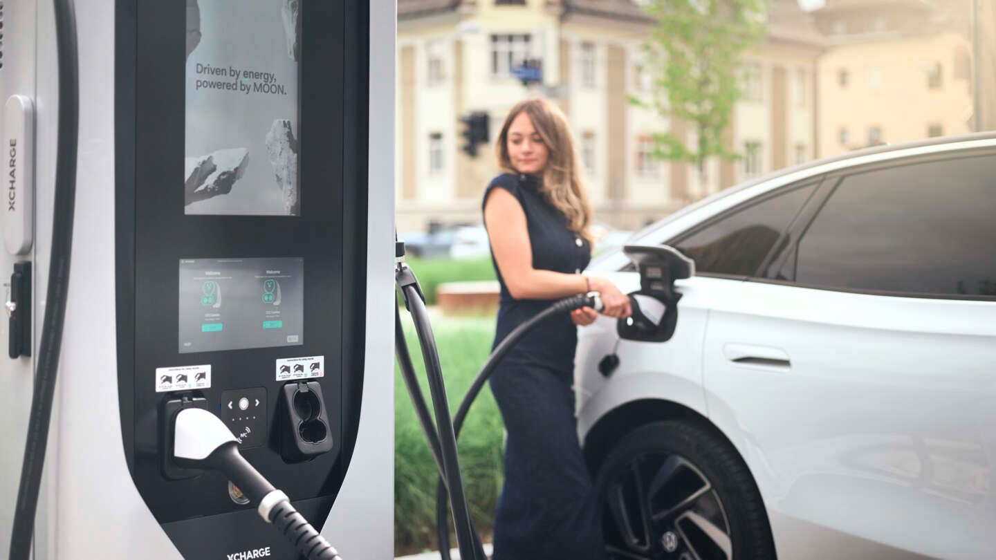 Frau lädt einen weißen VW ID.7 per MOON Ladestation mit Strom.