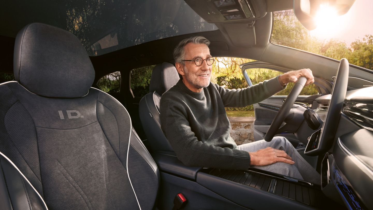 Ein Mann, der lächelt, sitzt auf dem Fahrersitz eines VW ID.7 Tourer und schaut durch die Frontscheibe auf einen Wald.