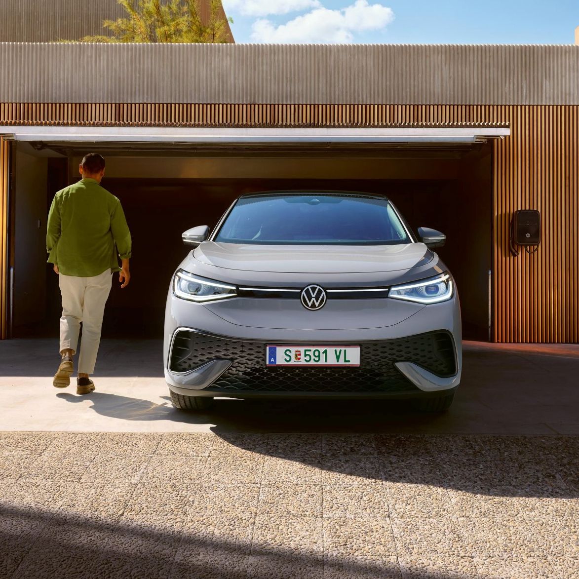 Ein grauer VW ID.5 steht vor einer Garage mit geöffnetem Tor. Ein Mann geht darauf zu.