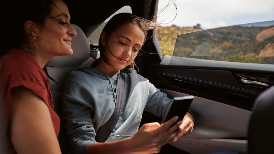 Zwei Frauen sitzen auf Rückbank eines VWs ID.7 und sehen sich am Smartphone einen digitalen Katalog an