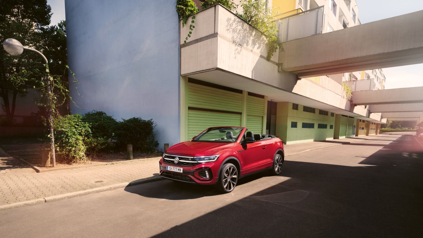 Roter T-Roc Cabriolet steht geparkt am Straßenrand neben dem Gehsteig in einer Stadt.