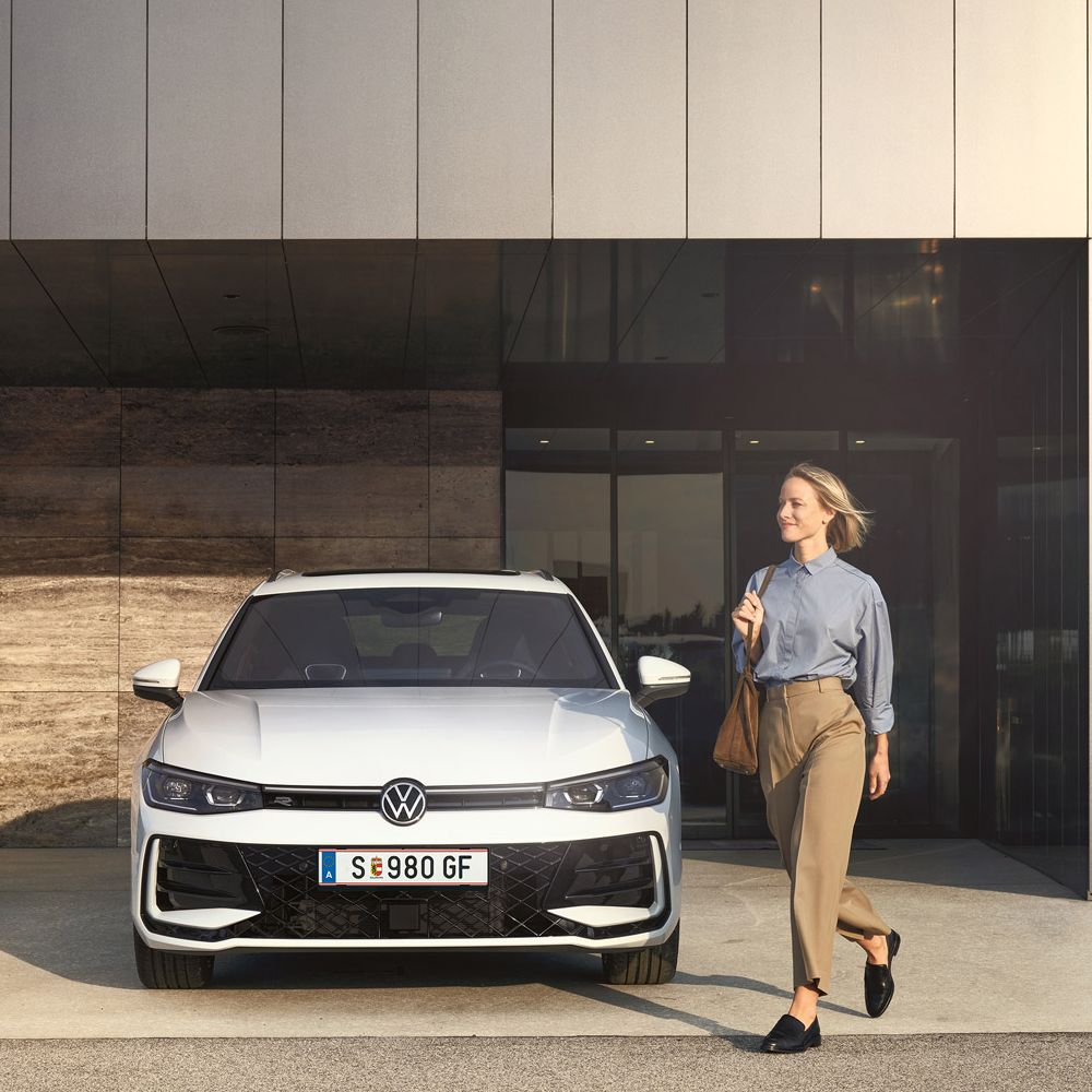 Frontansicht eines weißen VW Passat R-Line, eine Frau geht an ihm vorbei.