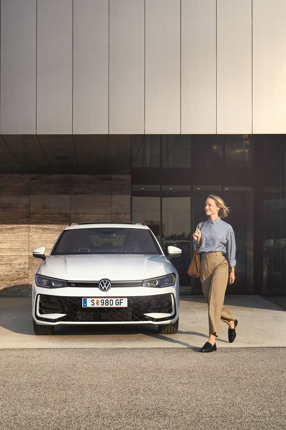 Frontansicht eines weißen VW Passat R-Line, eine Frau geht an ihm vorbei.