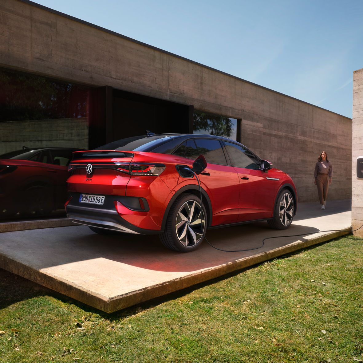 Ein roter VW ID.5 GTX lädt an einer Wallbox neben einem Bungalow mit großer Glasfront.