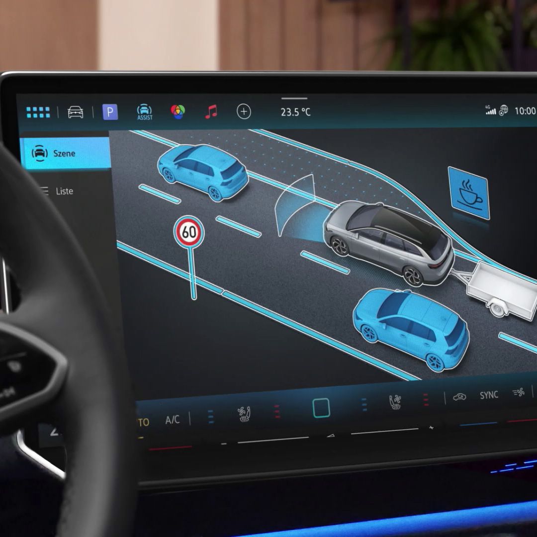 Das Bild zeigt das Display eines Fahrzeug-Infotainmentsystems. Es zeigt ein animiertes Beispiel für das rückwärtige Sicht-Assistenzsystem, das Autos und ein Straßenschild für Geschwindigkeitsbegrenzung anzeigt. Die Details beinhalten ein Fahrzeug, das einen Anhänger zieht, und die Temperaturanzeige des Fahrzeugs.