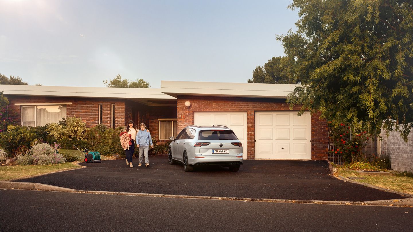 VW Golf Variant parkt in der Auffahrt eines Bungalow. Mutter und Tochter gehen aus dem Haus.