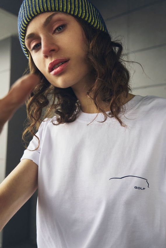 Eine junge Frau mit einem weißen T-Shirt mit aufgedrucktem Golf Logo.