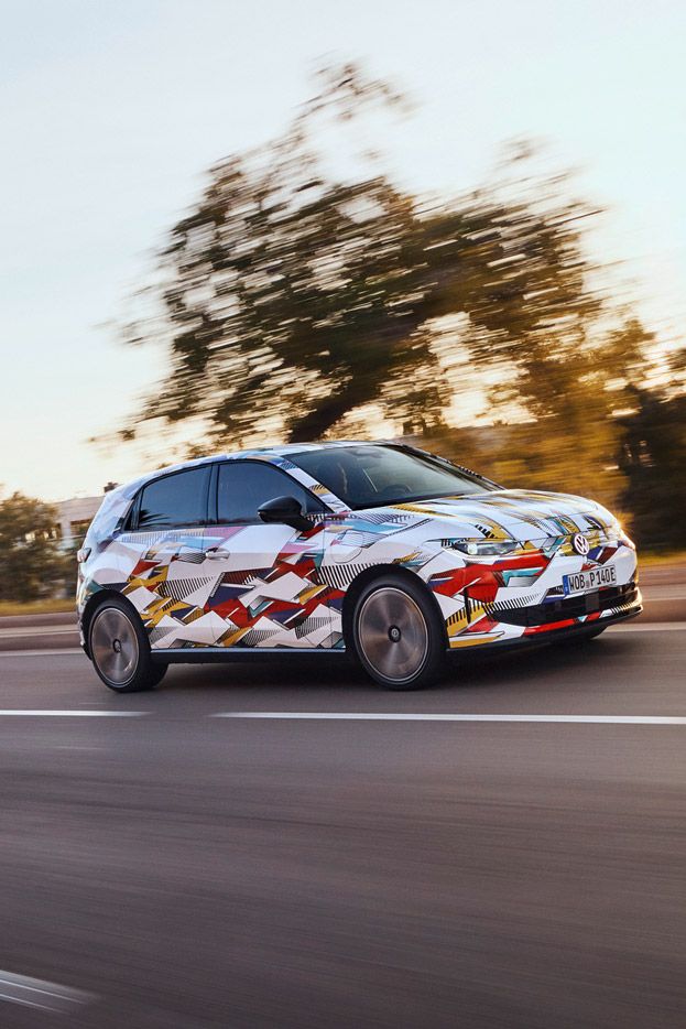 Ein ID. Polo fährt schnell auf einer Straße, umgeben von verschwommenen Bäumen und Landschaft bei Sonnenuntergang. Das Fahrzeug trägt eine auffällige, bunte Tarnlackierung. Die Straße ist leer und scheint sich durch eine ländliche Gegend zu schlängeln.