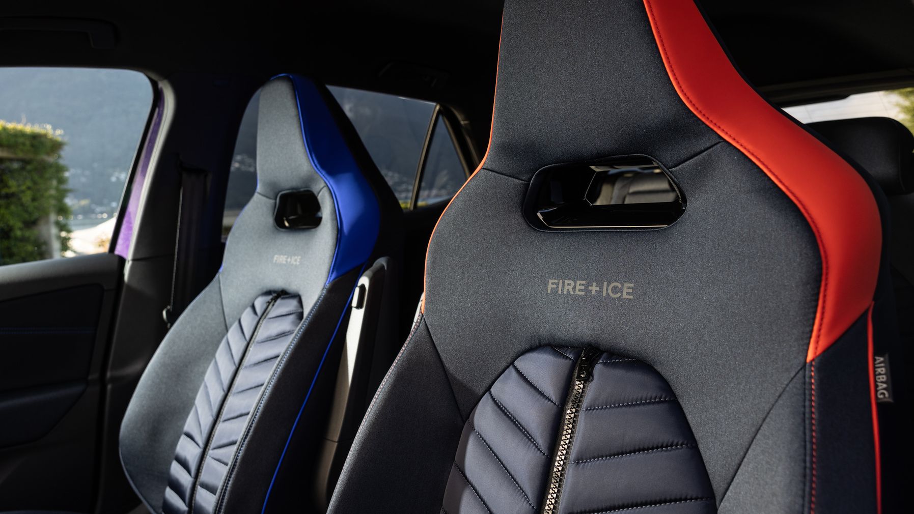Zwei Autositze mit sportlichem Design, der linke Sitz hat blaue Akzente, der rechte rote. Beide Sitze zeigen die Aufschrift "FIRE+ICE". Sie befinden sich im Inneren eines Fahrzeugs mit einem Fenster bei Tageslicht.