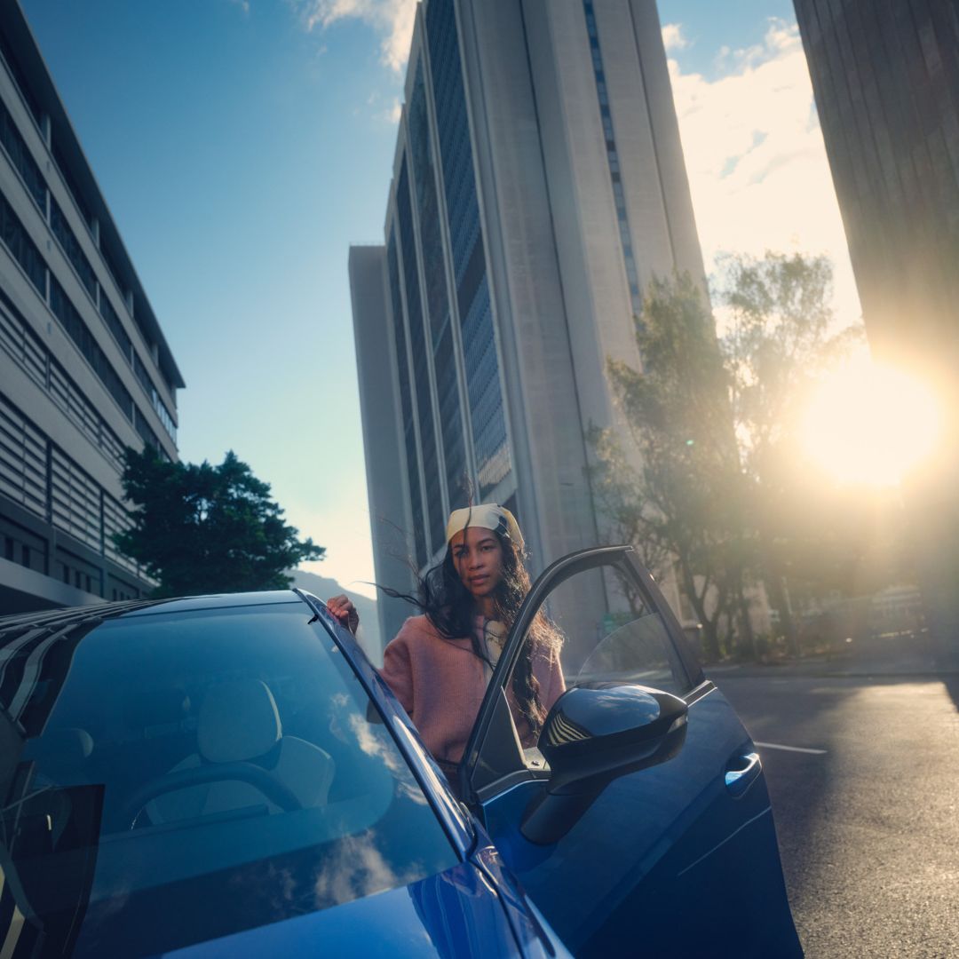 Ein blauer VW ID. Polo Style parkt in einer Stadt im Sonnenuntergang, eine Frau steigt auf der Fahrerseite aus.