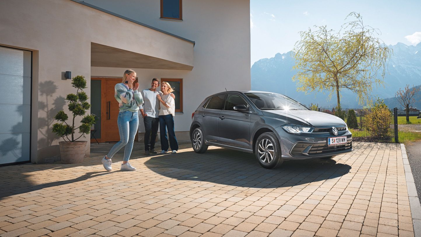 Polo steht geparkt vor einem Haus mit einer Familie im Hintergrund.