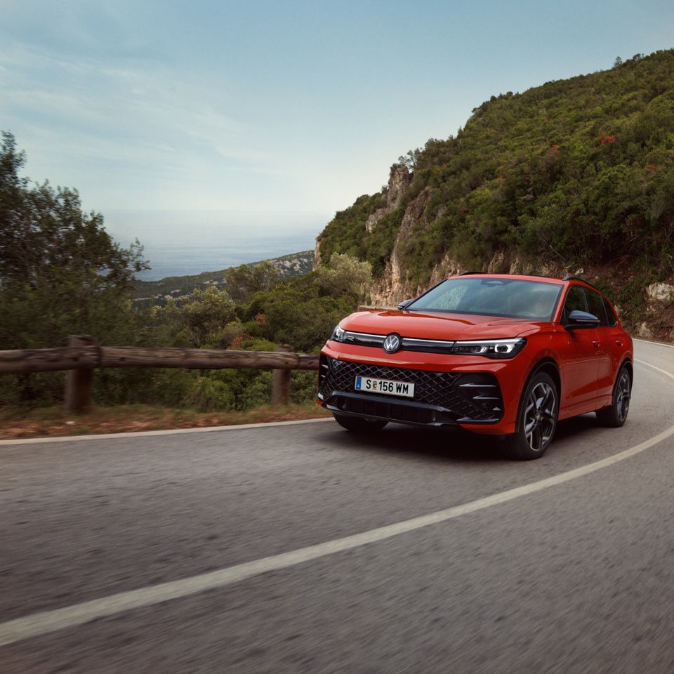 Roter VW Tiguan R-Line fährt eine kurvige Straße entlang.