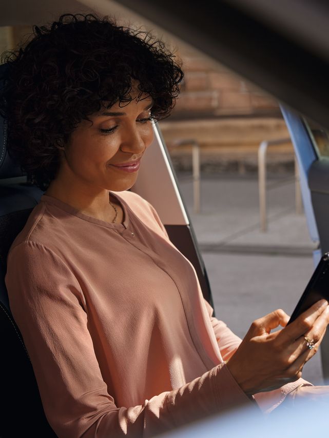 Eine lächelnde Frau schaut auf dem Fahrersitz eines geparkten VW T-Cross aufs Handy.