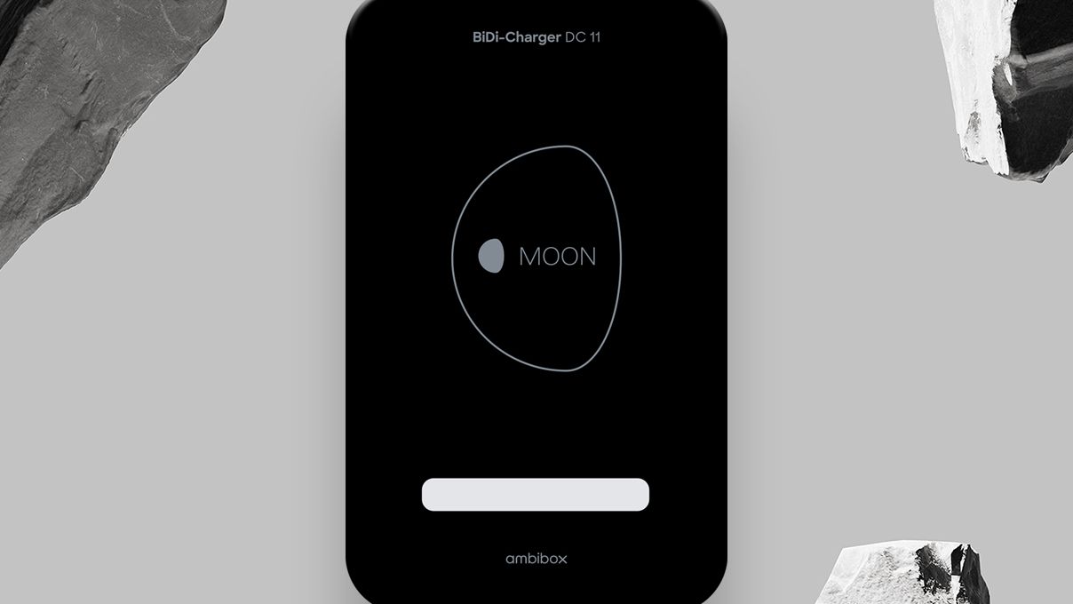 Ein BiDi-Ladegerät DC 11 mit einem eleganten schwarzen Design und dem Schriftzug "MOON" in der Mitte, umgeben von einer Kontur. Es befindet sich vor einem grauen Hintergrund mit zwei großen, strukturierten Steinen an den Seiten.