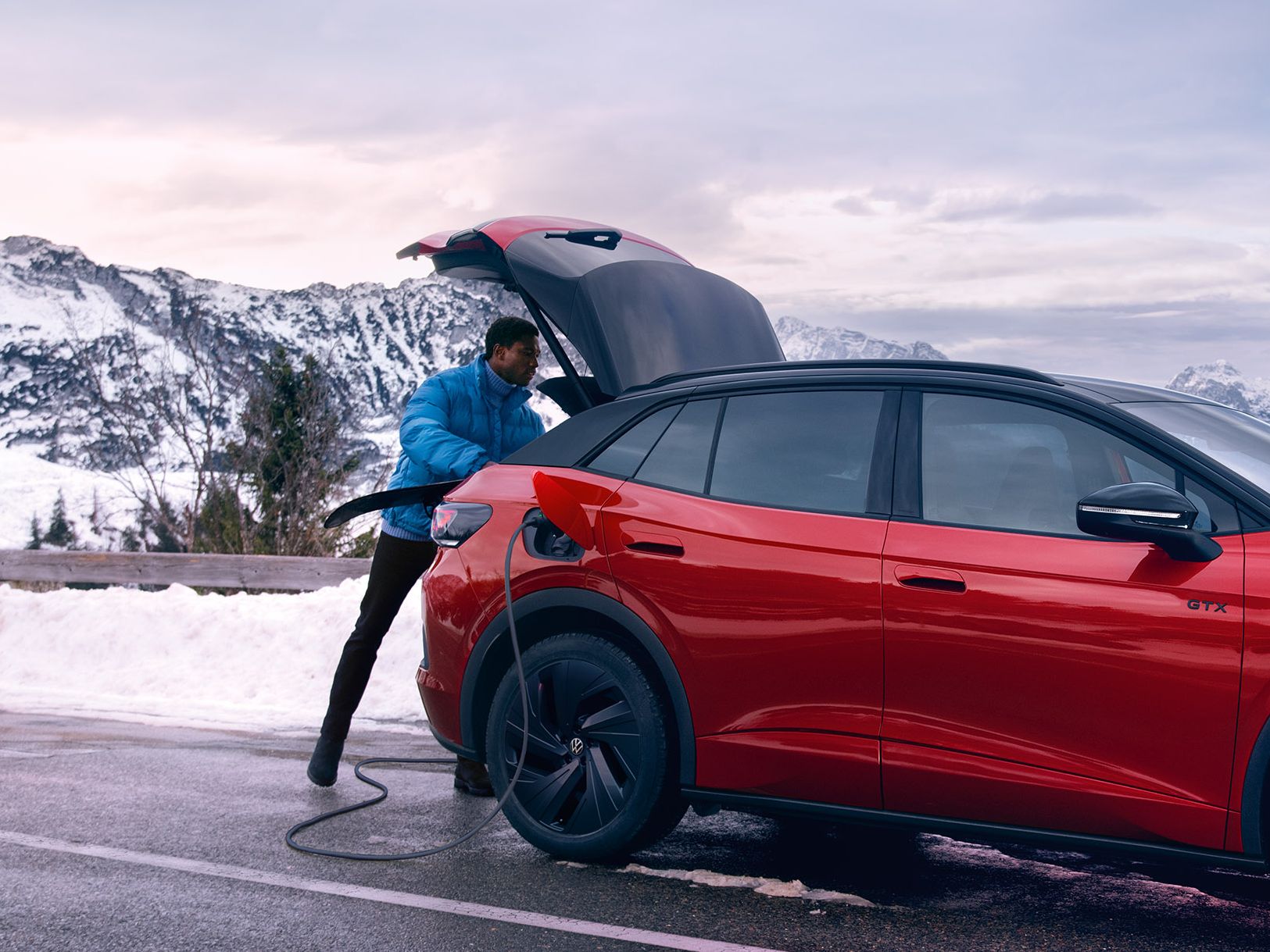 Mann öffnet Kofferraum eines VW ID.4 GTX auf einer Bergstraße