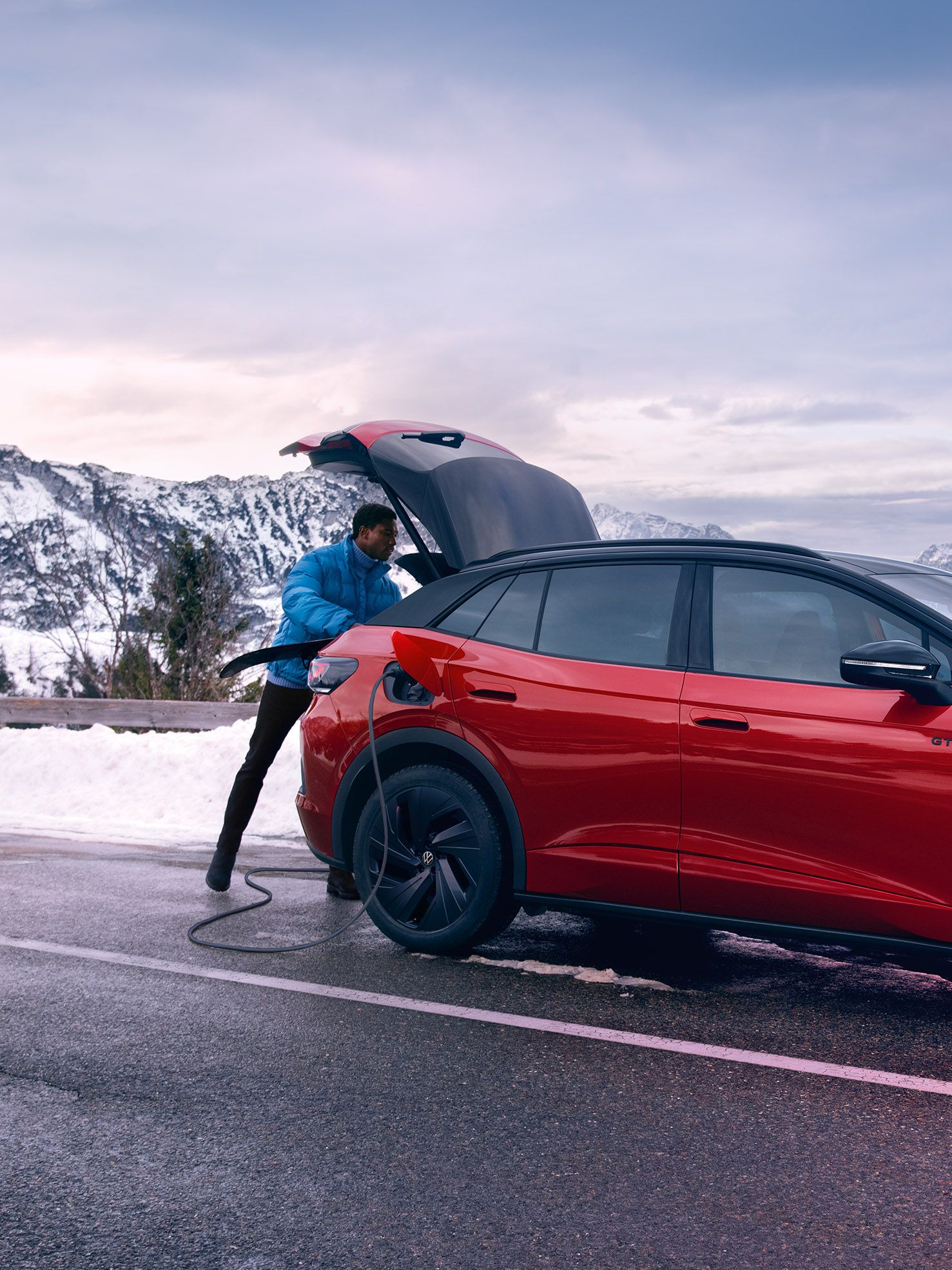 Mann öffnet Kofferraum eines VW ID.4 GTX auf einer Bergstraße