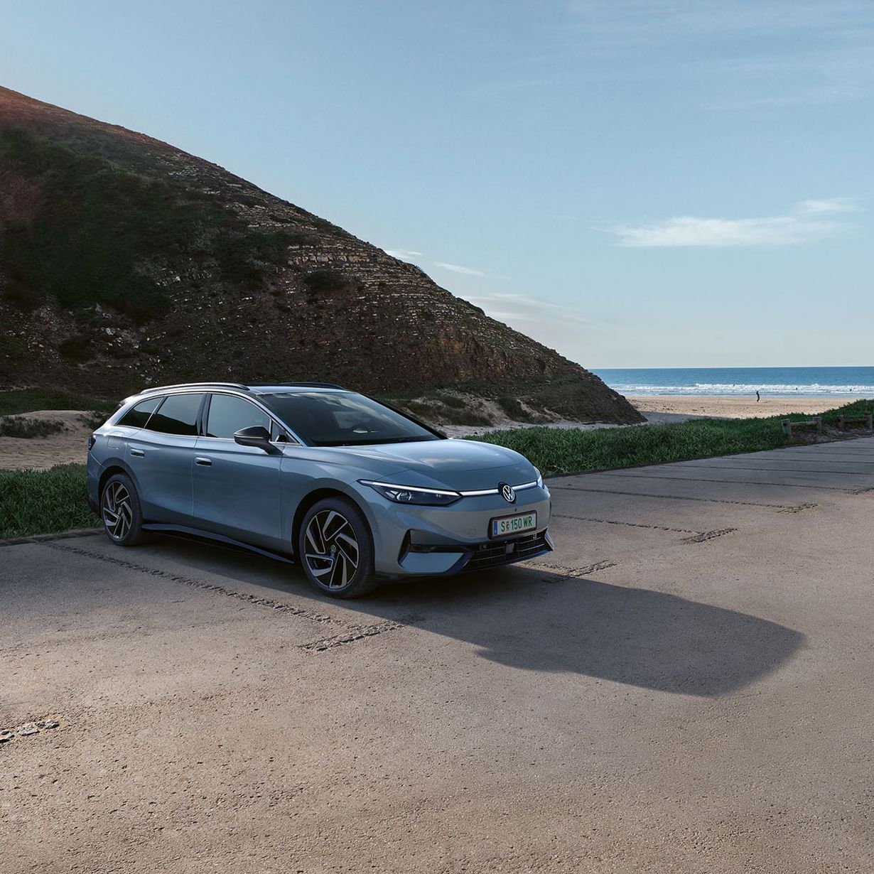 Ein geparkter ID.7 Tourer neben einem Hügel mit Strand und Meerblick im Hintergrund.