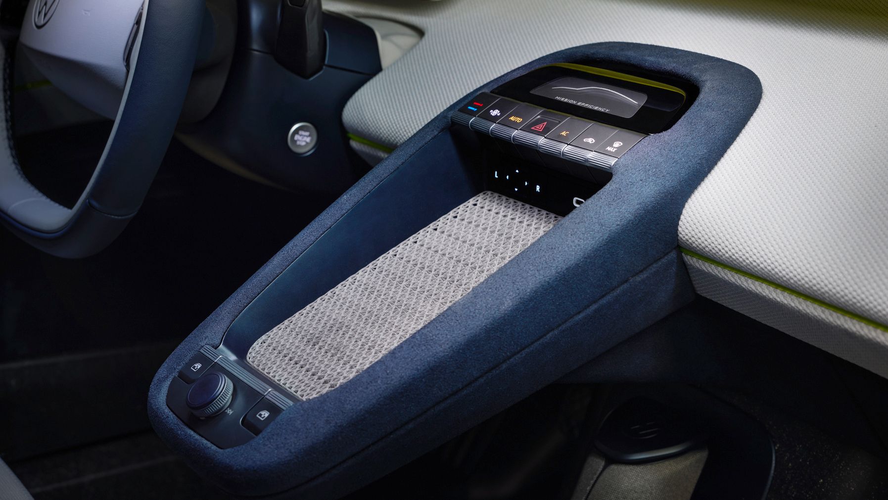 Modernes Auto-Innenraumdetail mit Fokus auf der schwebenden Mittelkonsole in blauem Stoff und heller Ablagefläche. Zu sehen sind eine Touch-Bedienleiste mit Symbolen für Klima- und Fahrzeugfunktionen sowie ein Drehregler in der Nähe des Fahrersitzes. Links ist der Lenkradbereich mit einem digitalen Display teilweise erkennbar.