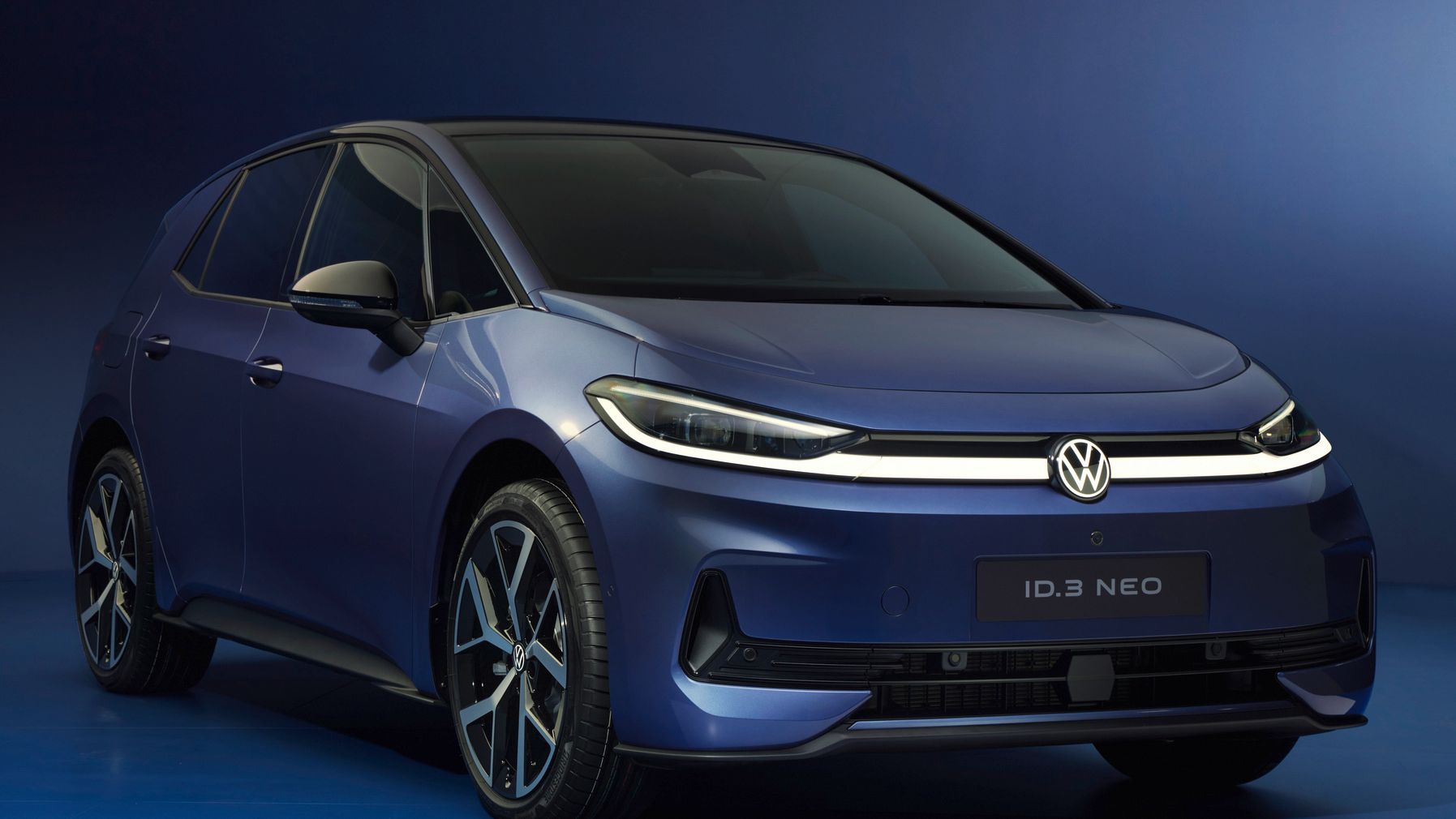 Blaues Volkswagen-Elektroauto des Modells ID.3 Neo vor blauem Hintergrund, leicht von vorne links aufgenommen. Das Fahrzeug hat eine glatte, aerodynamische Front mit schmalen LED-Scheinwerfern und einem durchgehenden Lichtband. Moderne, zweifarbige Felgen unterstreichen das sportliche Design.