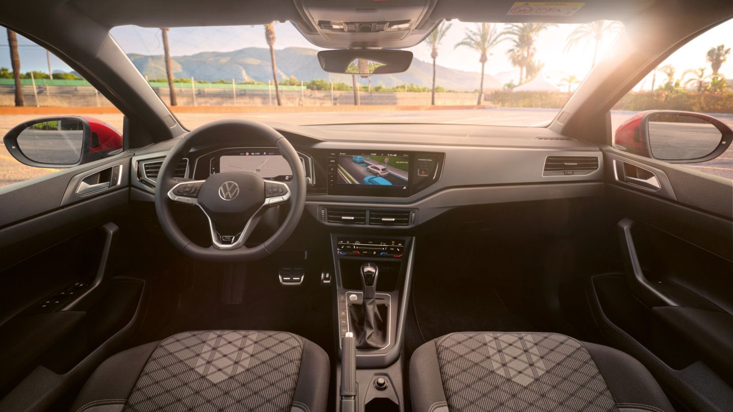 Blick auf das Cockpit mit Lenkrad und Infotainment-System im VW Taigo. Vor dem Fahrzeug sind Palmen und Berge.
