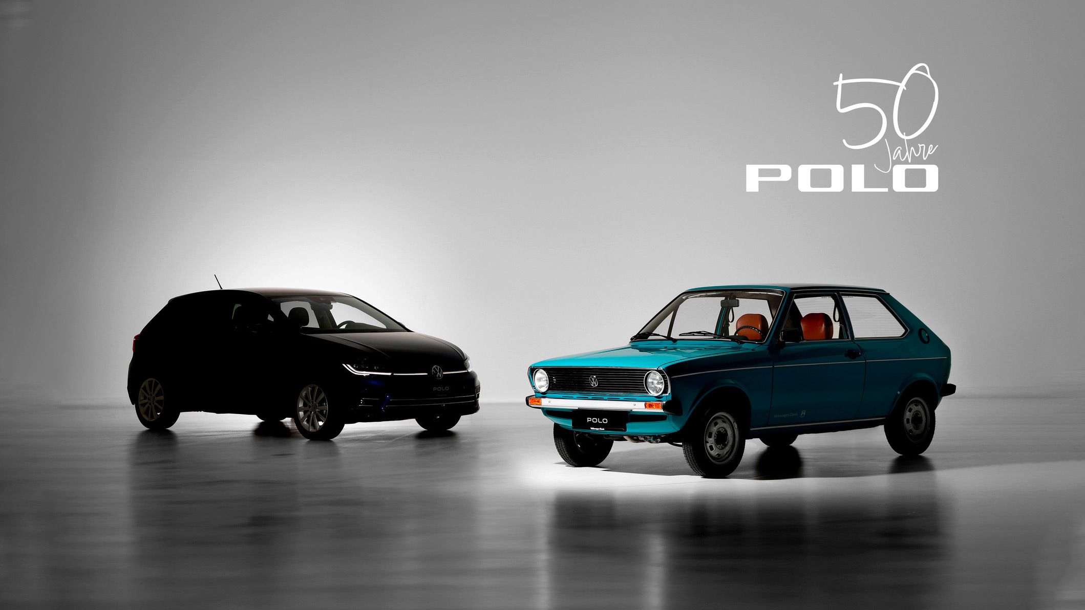 Zwei Volkswagen Polo Modelle nebeneinander: ein moderner schwarzer Polo und ein klassischer blauer Polo aus den frühen Jahren. Im Hintergrund steht „50 Jahre Polo“ geschrieben. Beleuchtung betont die Unterschiede zwischen den beiden Fahrzeugen.