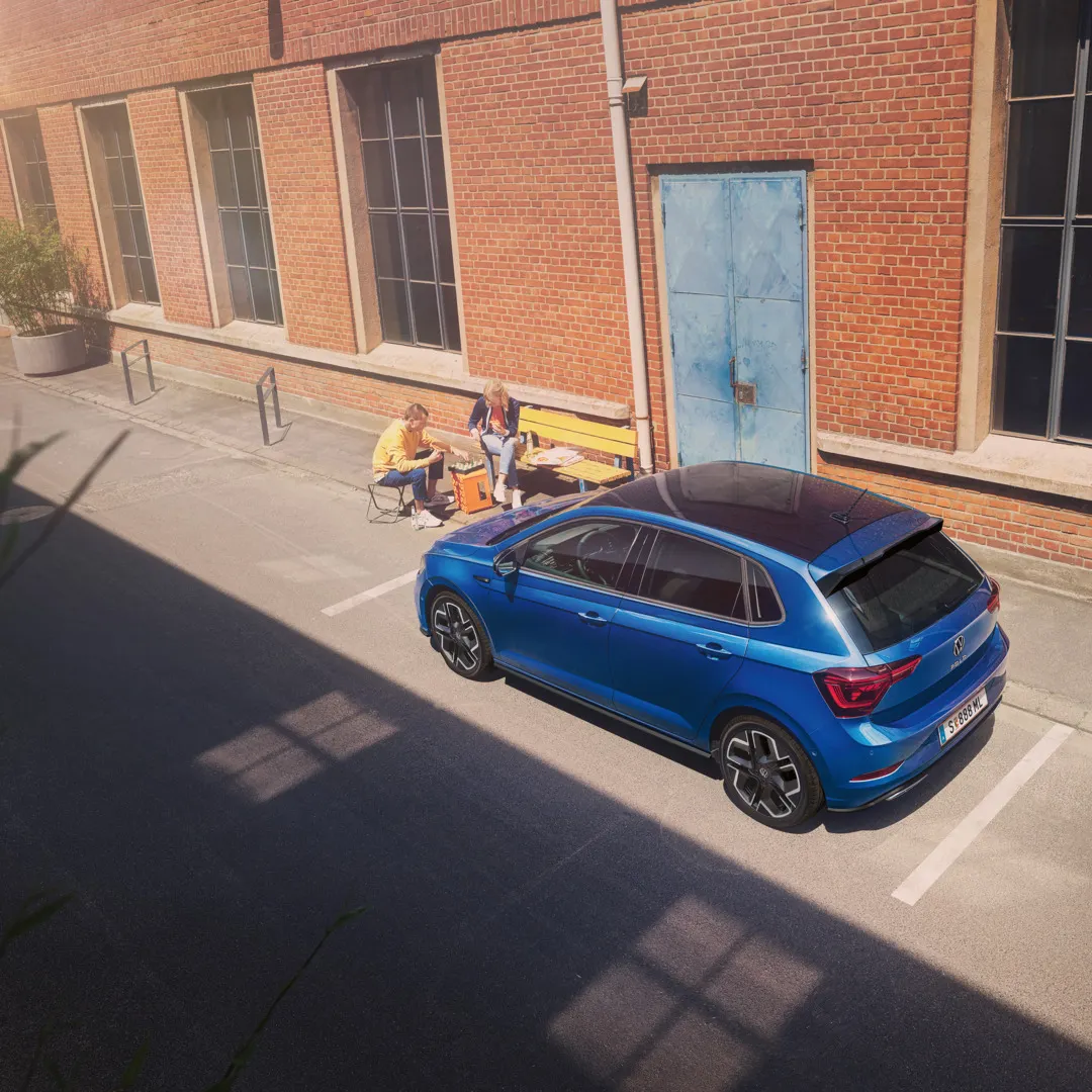Blick von schräg oben auf einen parkenden VW Polo R-Line mit Roof-Pack, neben dem Auto spielt ein Pärchen Schach.