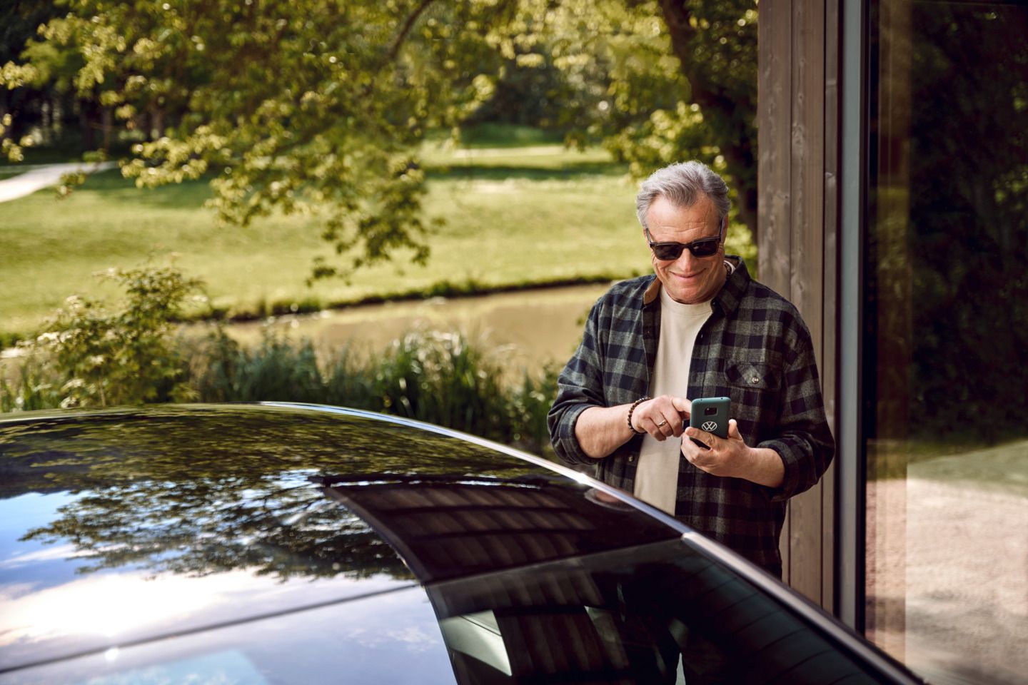 Ein Mann steht hinter einem VW und hält ein Handy in der Hand.  